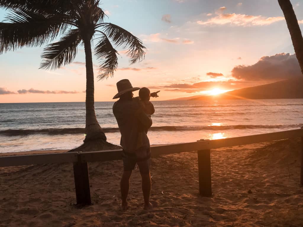 Dad pointing at sunset while holding baby in Maui, Hawaii.