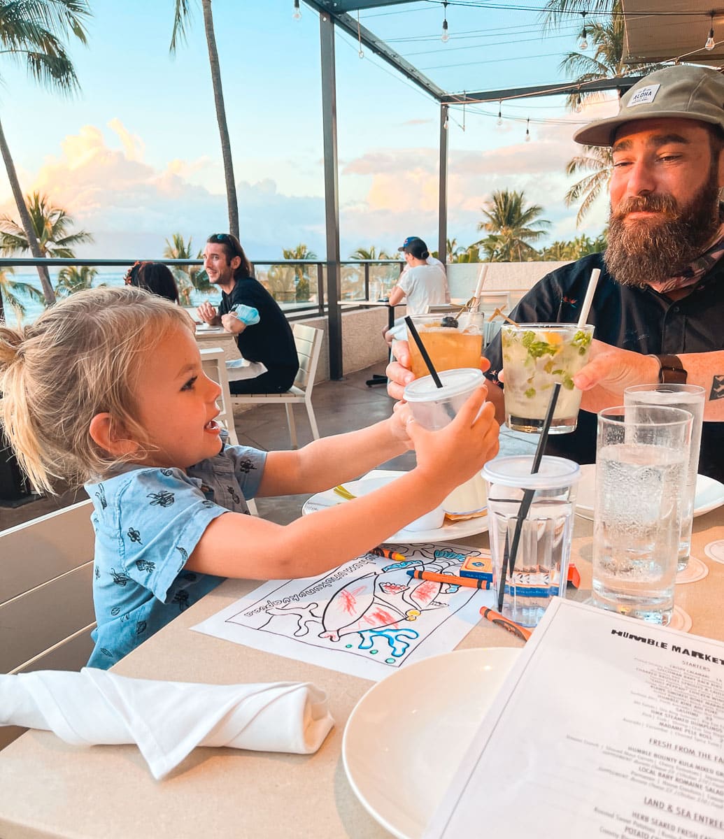 A toddler cheersing dad at family-friendly restaurant on Maui. 