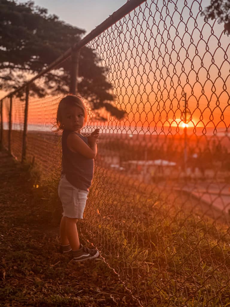 Toddler watching the sunset from behind a fence in Maui, Hawaii. 