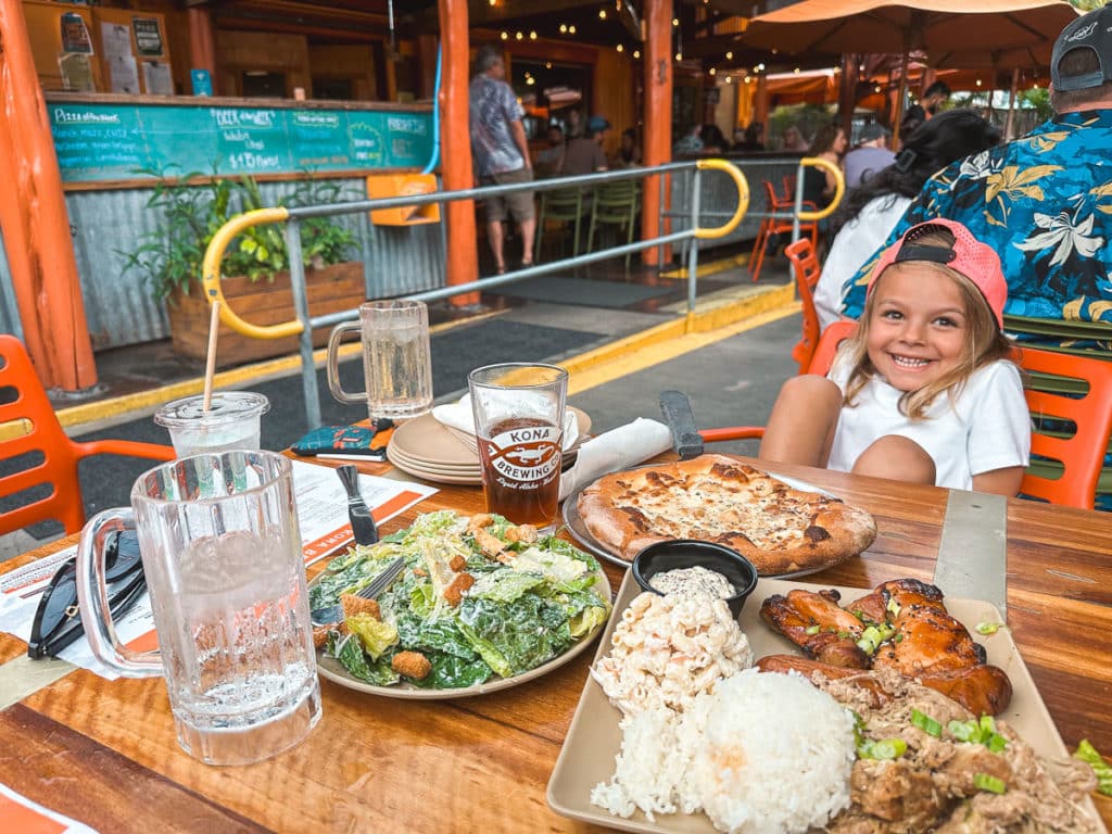 A kid smiling at a table full of food at Kona Brewing Company, Big Island, Hawaii