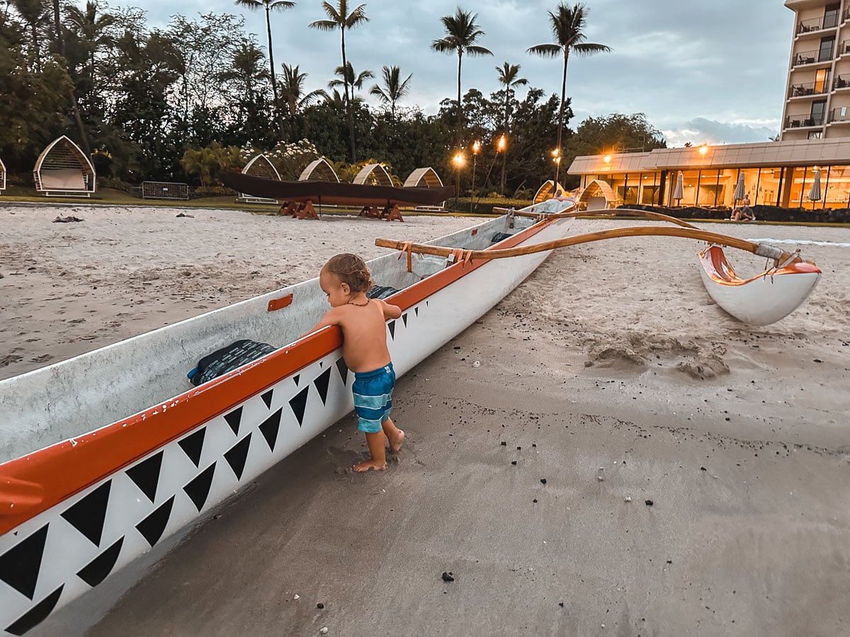 Toddler exploring an outrigger canoe on the beach at Mauna Lani resort Big Island Haw