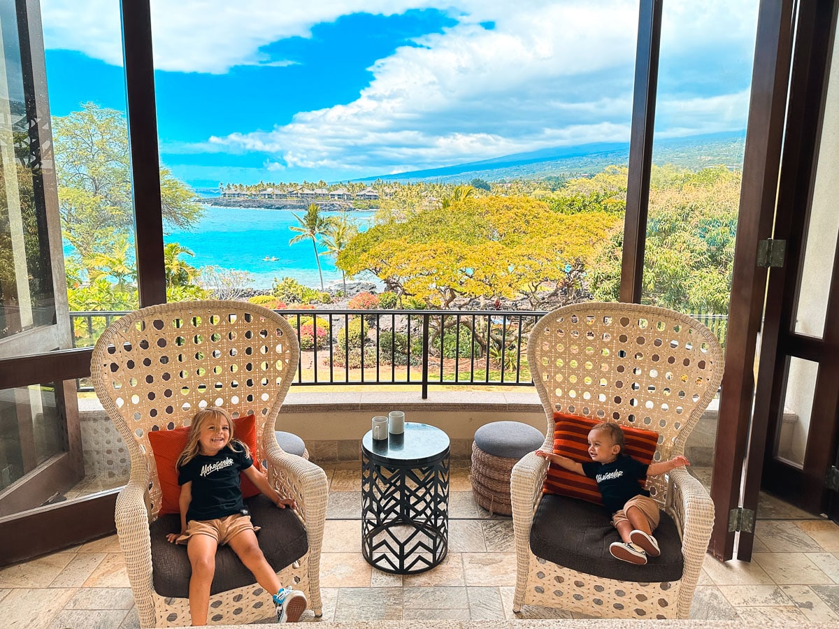 Two kids sitting on a lanai at Outrigger Kona Resort with ocean views in the background, Big Island Hawaii