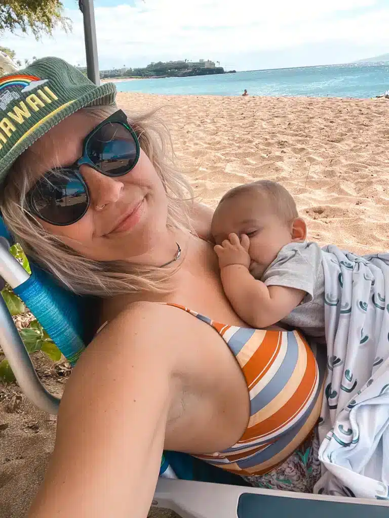 A mom with a sleeping baby on her chest on a beach in Maui, Hawaii.