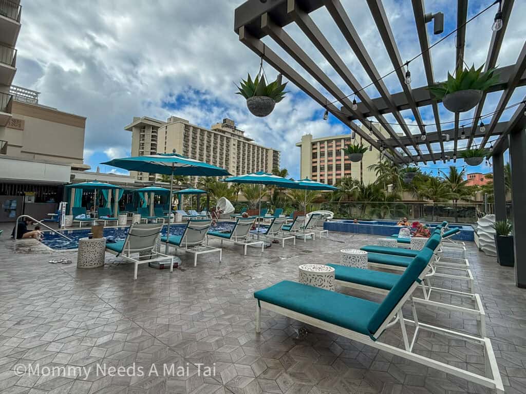 Rooftop pool at Waikiki Beachcomber by Outrigger with lounge chairs, umbrellas, and surrounding Waikiki hotels.