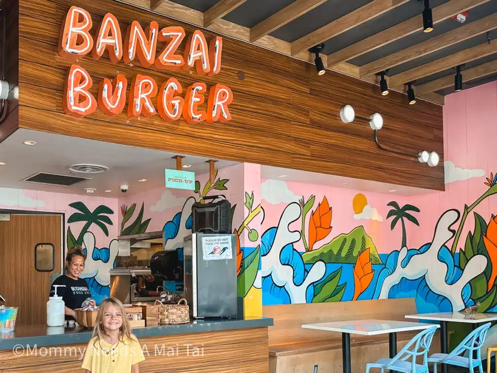 A child stands in front of a Banzai Burger sign with an employee smiling in the background in Waikiki, Hawaii.