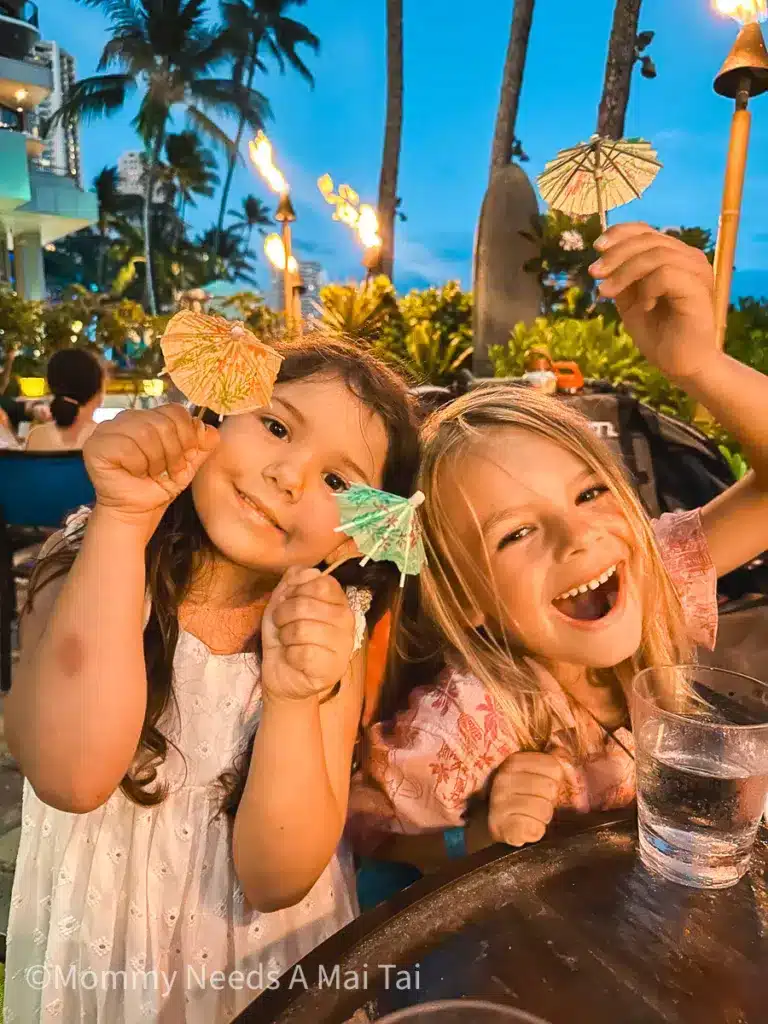 Two kids playing with drink umbrellas at Dukes Waikiki on Oahu, Hawaii. 