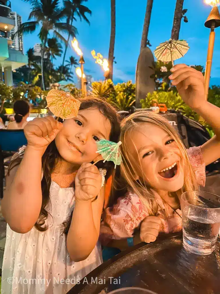 Two kids playing with drink umbrellas at Dukes Waikiki on Oahu, Hawaii.
