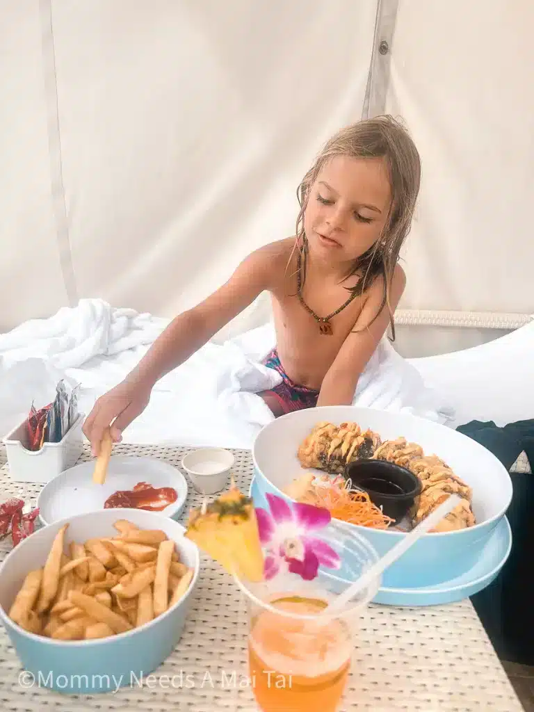 A boy with long hair dipping french fries in a cabana at a resort on Maui, Hawaii. 