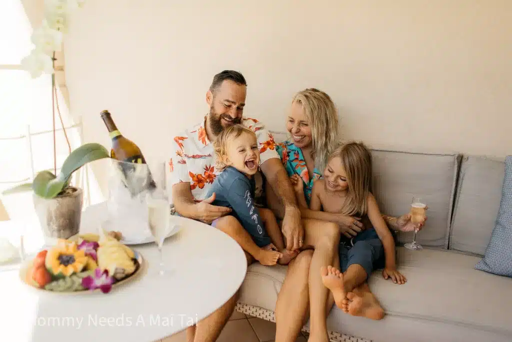 A family laughing while drinking champagne and playing with kids on a lanai at the Four Seasons Resort in Maui, Hawaii. 