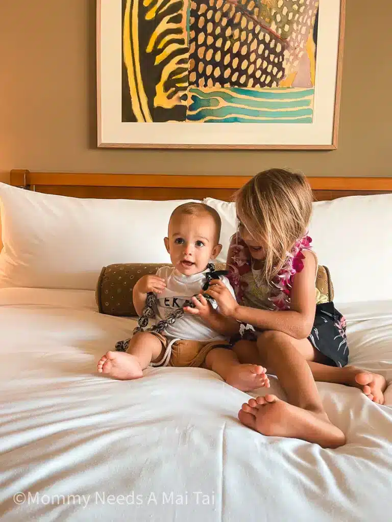 Two young kids wearing leis on a bed at Fairmont Kea Lani Resort in Maui, Hawaii. 