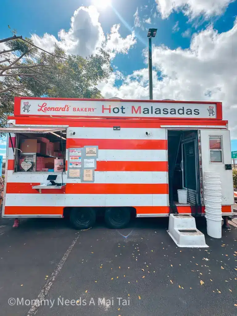 The outside of one of many "Malasadamobiles" located on Oahu, Hawaii. Sign reads "Leonard's Bakery: Hot Malasadas." Window is open and ready for business. 