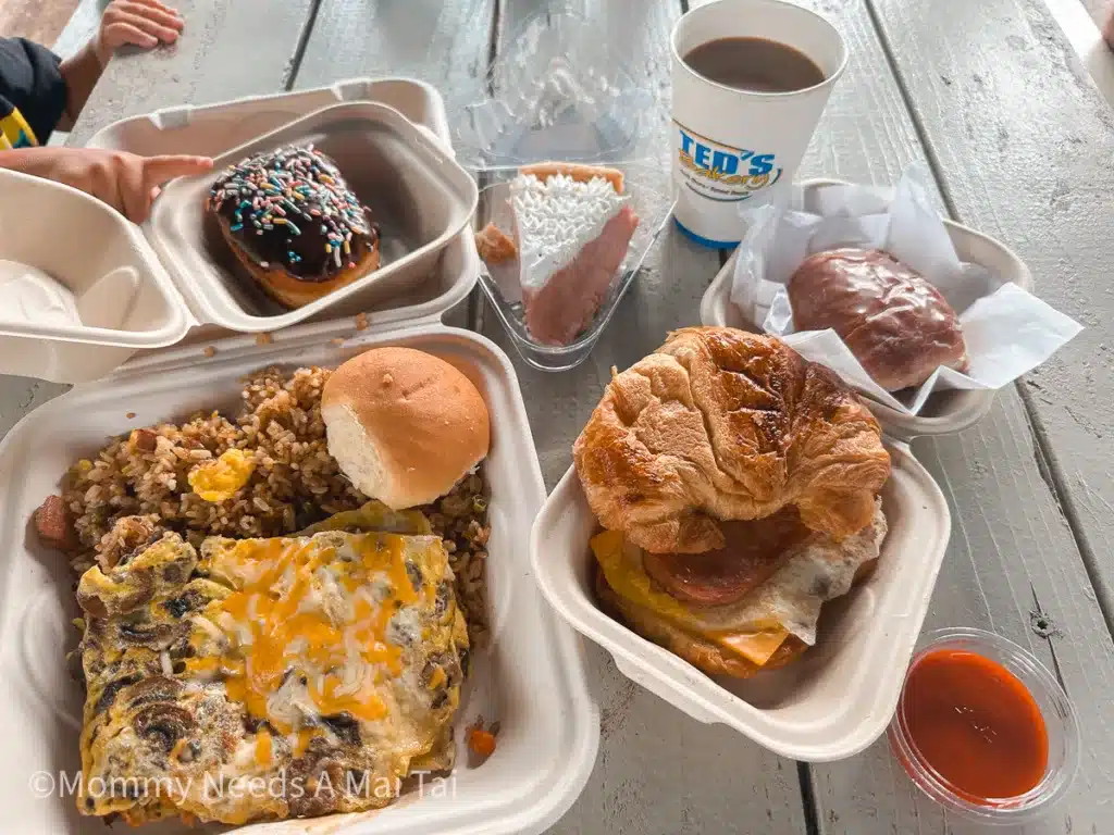 A large to go order from Ted's Bakery on North Shore, Oahu. Photo includes two donuts, a slice of pie, coffee, breakfast sandwich, and breakfast scramble with spam fried rice. 