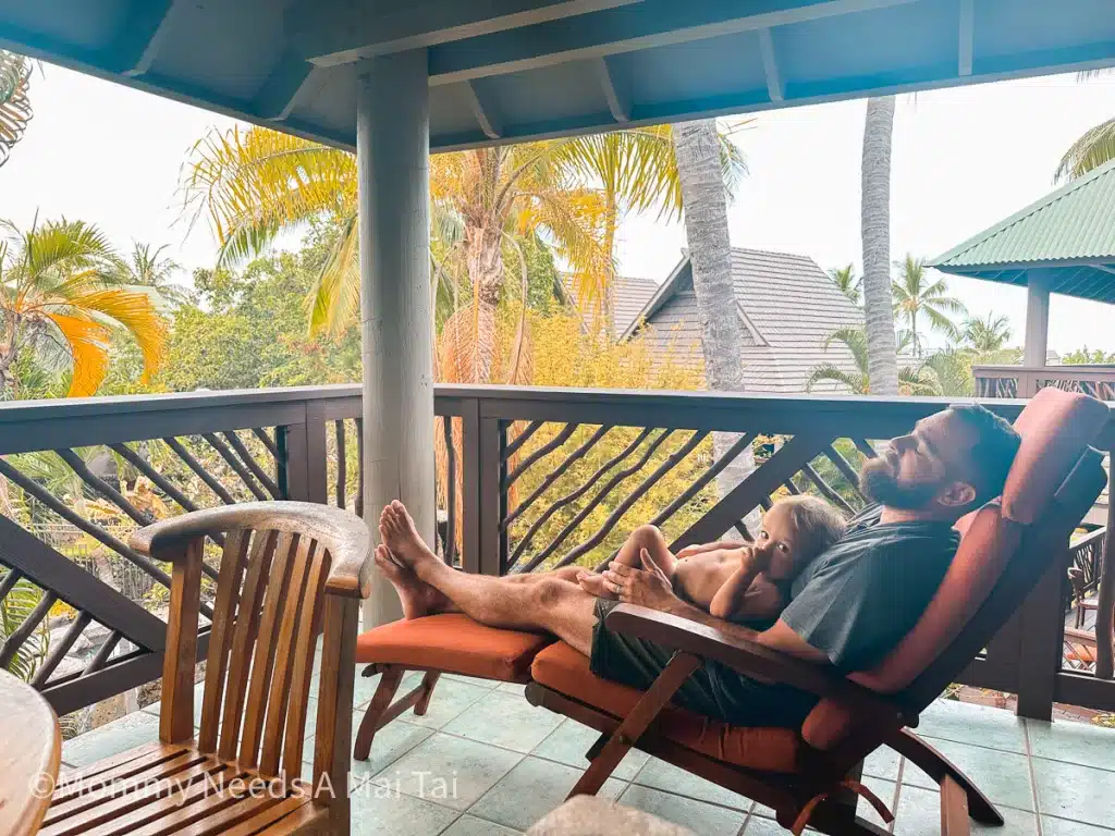 A dad closing his eyes while holding a toddler on a large vacation rental lanai in Hawaii. 
