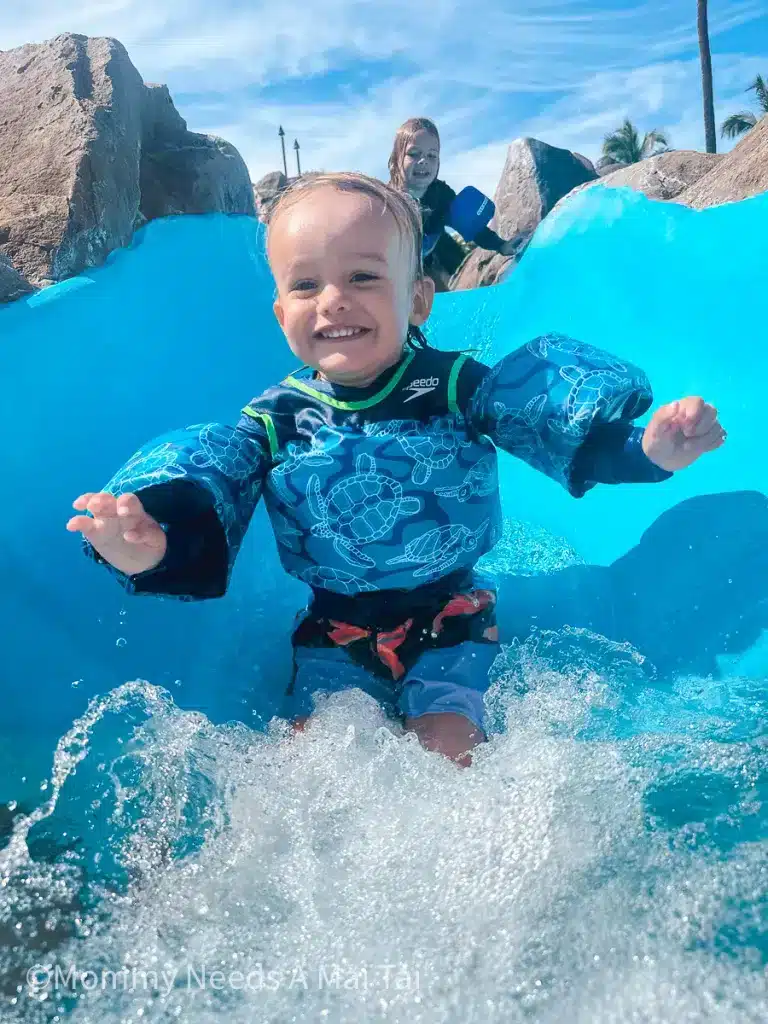 A young toddler going down a waterslide at a resort in Hawaii with his brother behind him. 