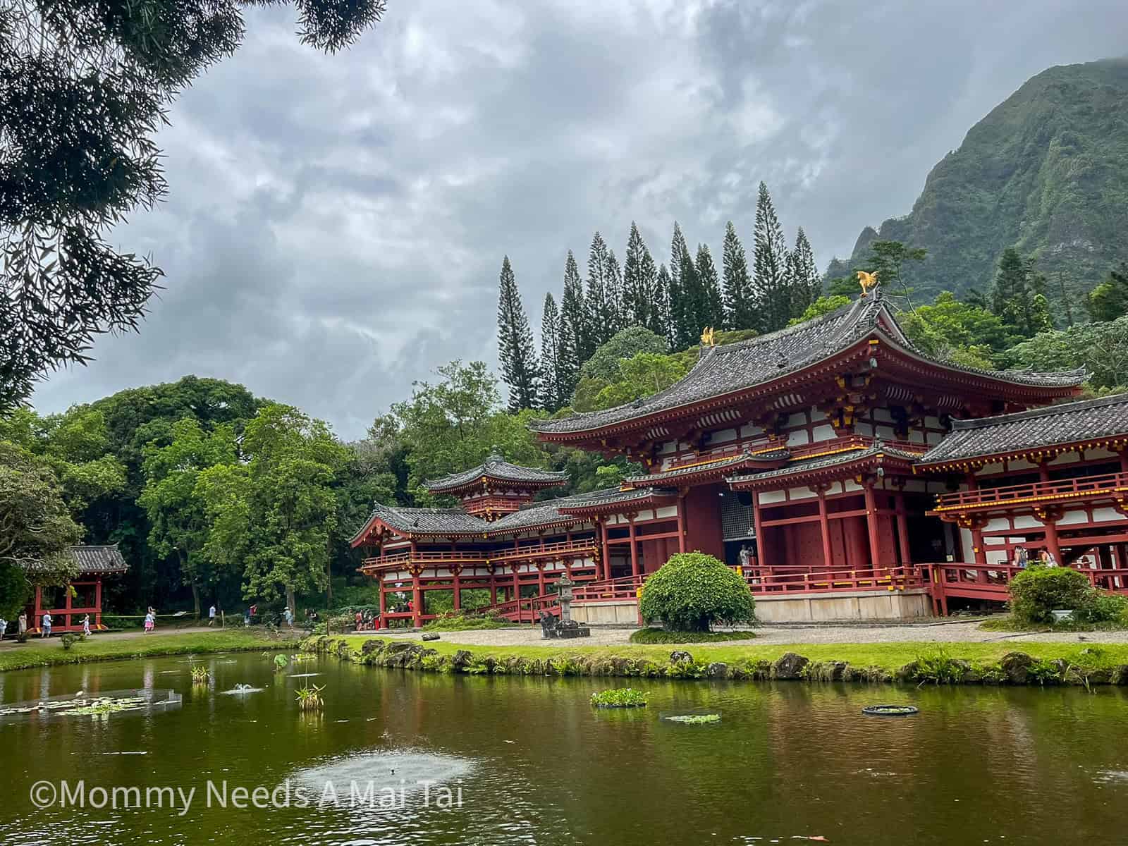 The Byodo-In Temple in Kaneohe, Oahu, reflected in a peaceful koi pond with lush green mountains in the background.