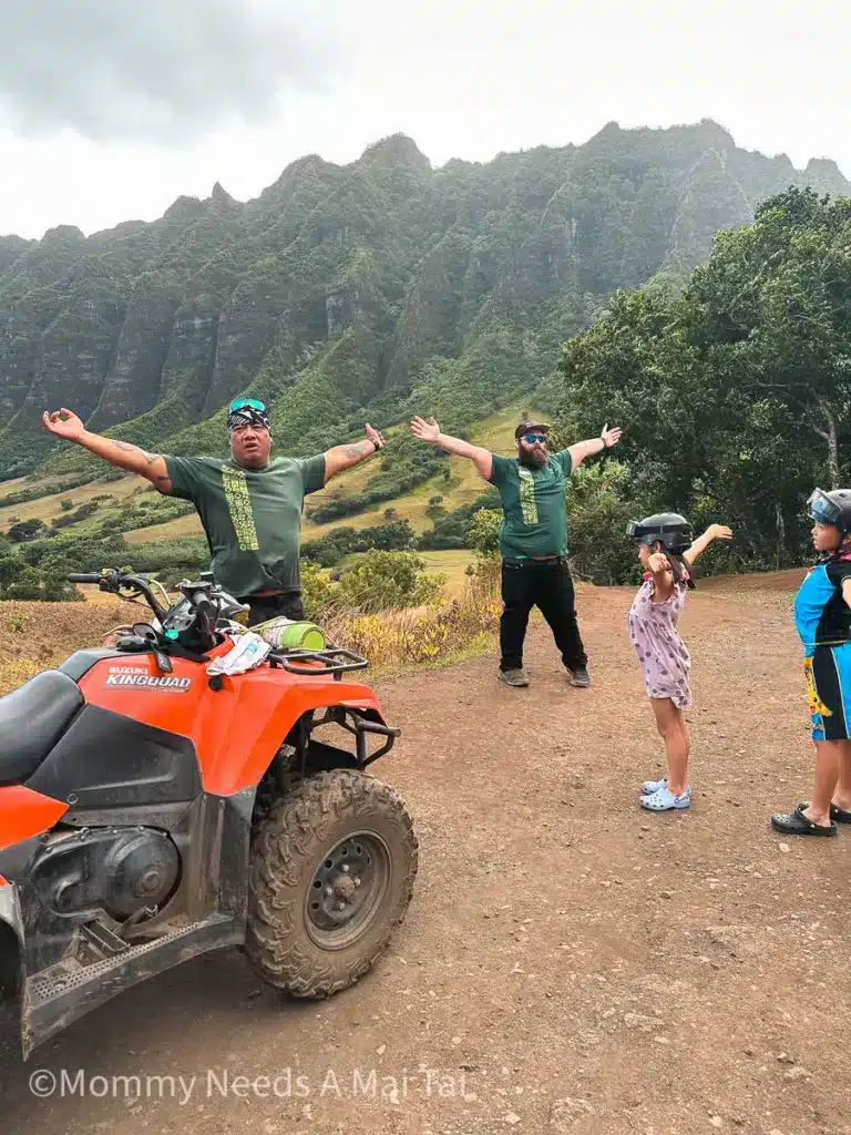 Two tour guides stand with their arms outstretched in front of children and UTVs at Kualoa Ranch in Oahu, Hawaii.