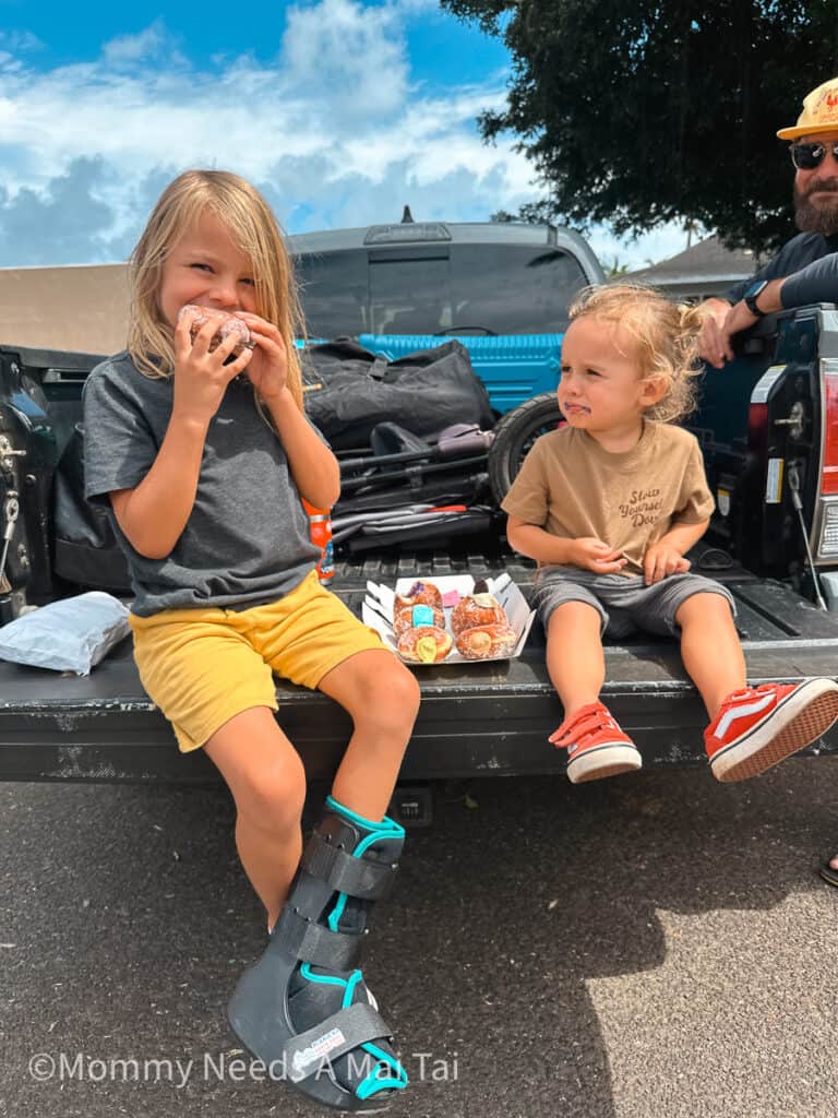 Two young boys and a smiling dad, sitting in the back of a truck eating Malasads on Kauai.