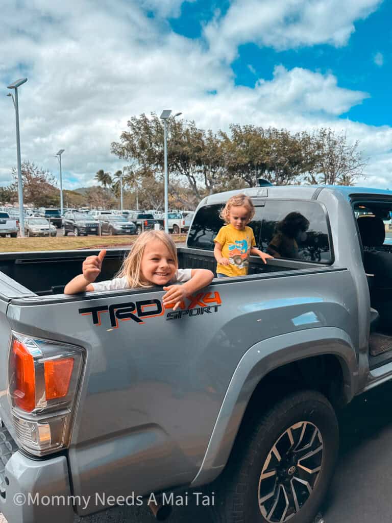 Two boys sitting in the back of a pickup truck giving shakas at the Lihue Airport on Kauai.