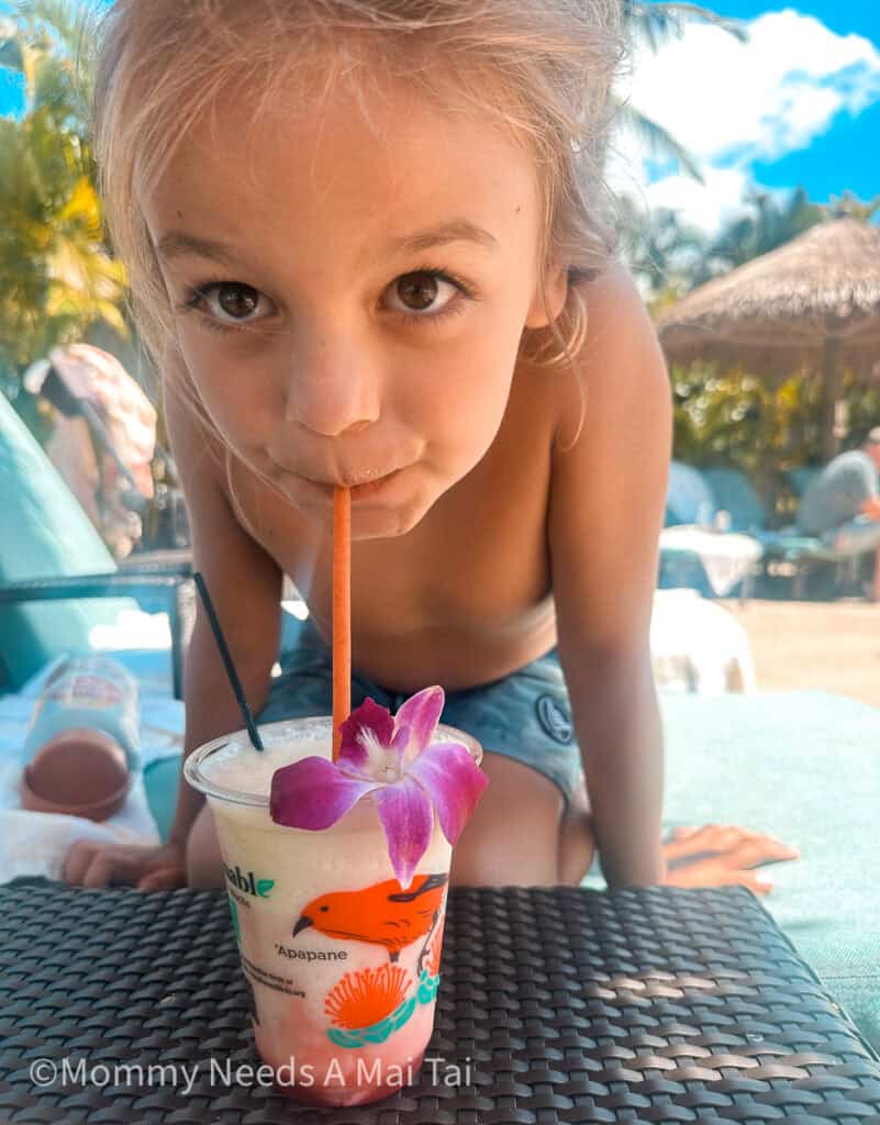 A young kid drinking a virgin pina colada by a resort pool on Kauai.