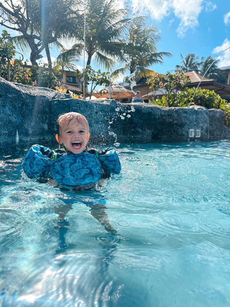 A toddler wearing floaties and laughing at Koloa Landing in Kauai, Hawaii.